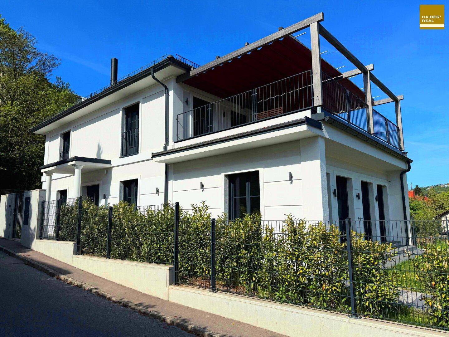 Neubau-Einfamilienhaus mit moderner Architektur, Balkon und gepflegter Gartenanlage an einer Straße.