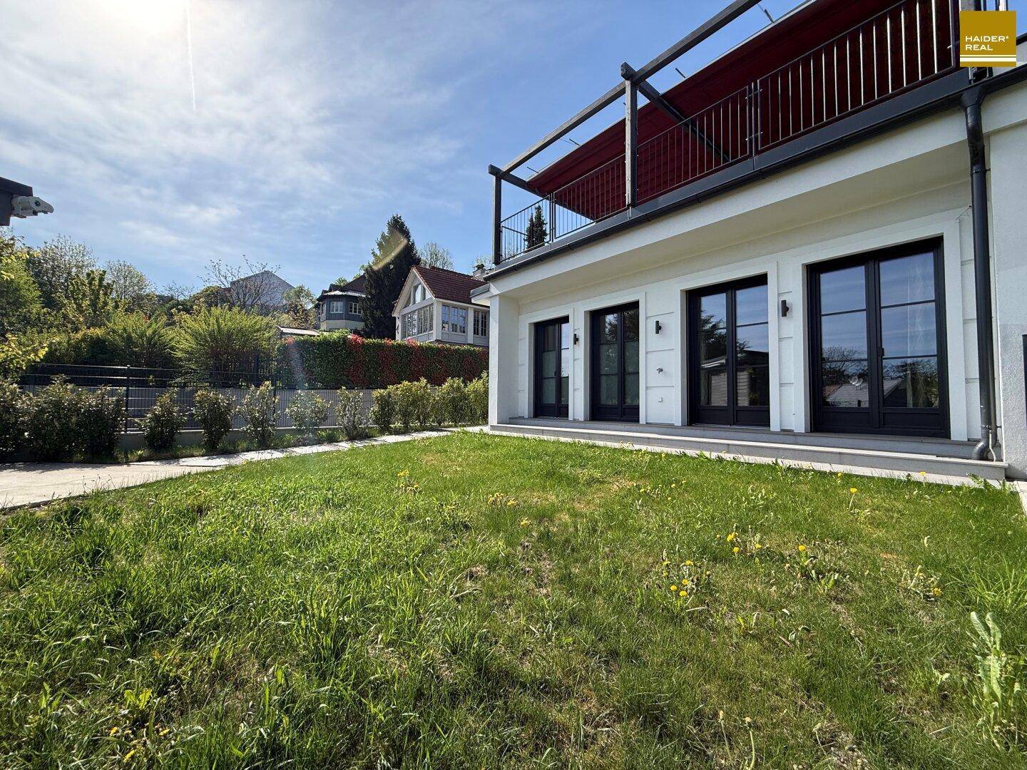 Gepflegter Rasenbereich hinter dem Haus mit Zugang zu großen Fenstern und einer oberen Terrasse.