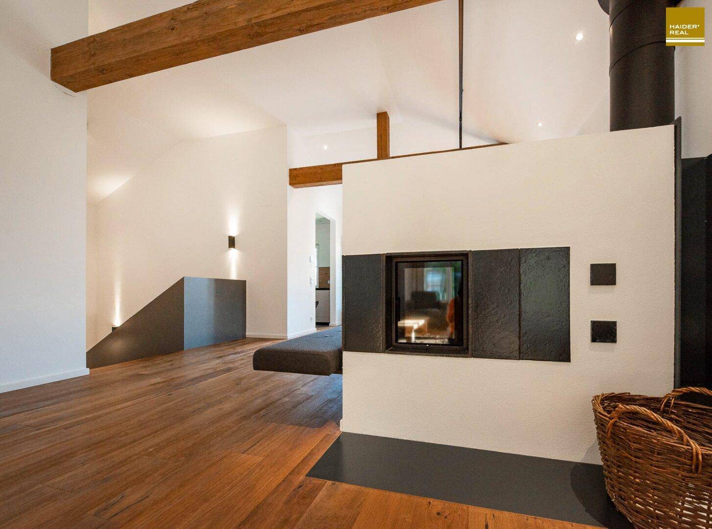 Helles Wohnzimmer mit Holzboden, sichtbaren Holzbalken und einem modernen Kamin als Mittelpunkt.