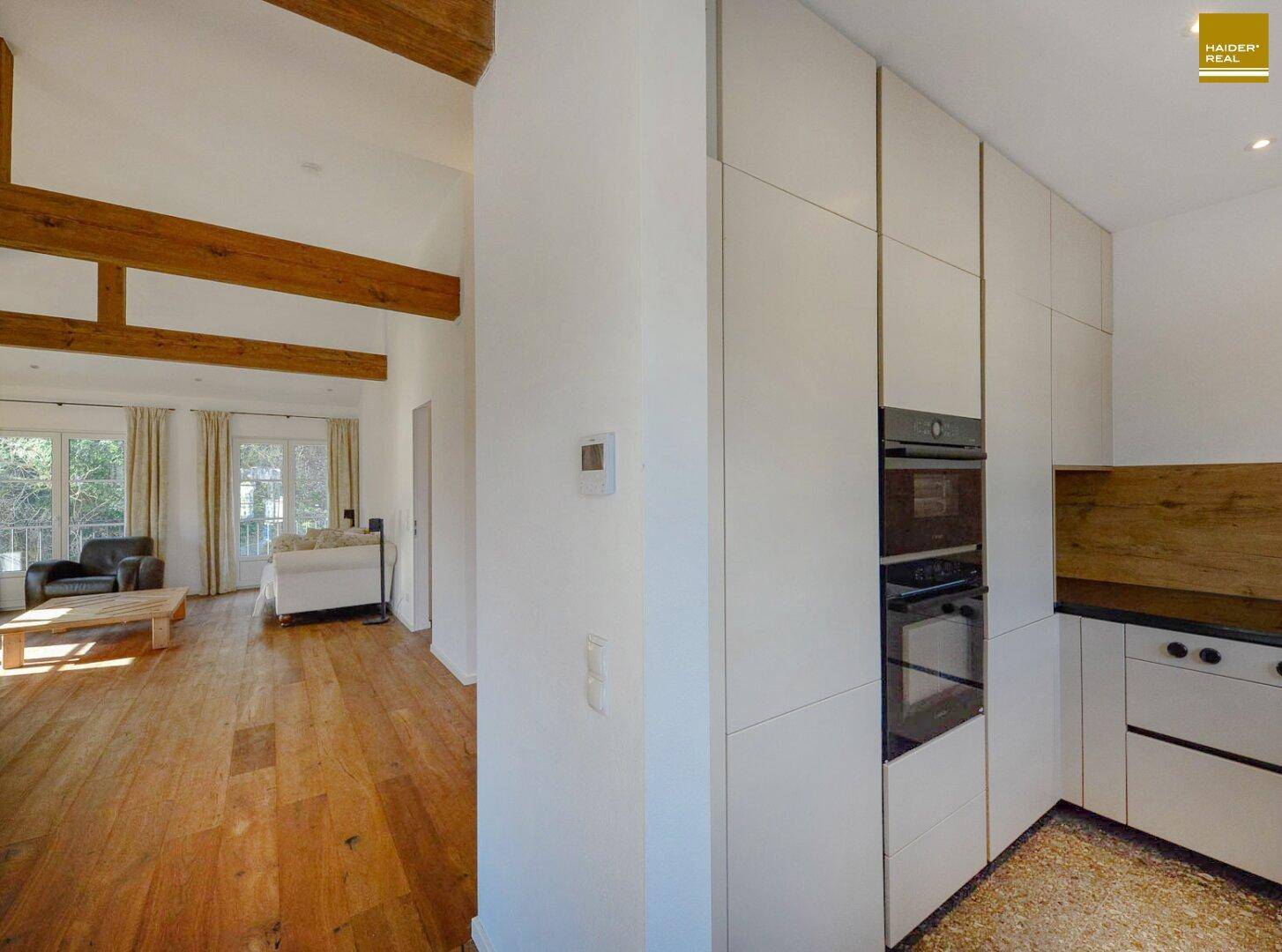 Moderne Einbauküche mit hellen Fronten, integrierten Geräten und Holzboden im offenen Wohnbereich.