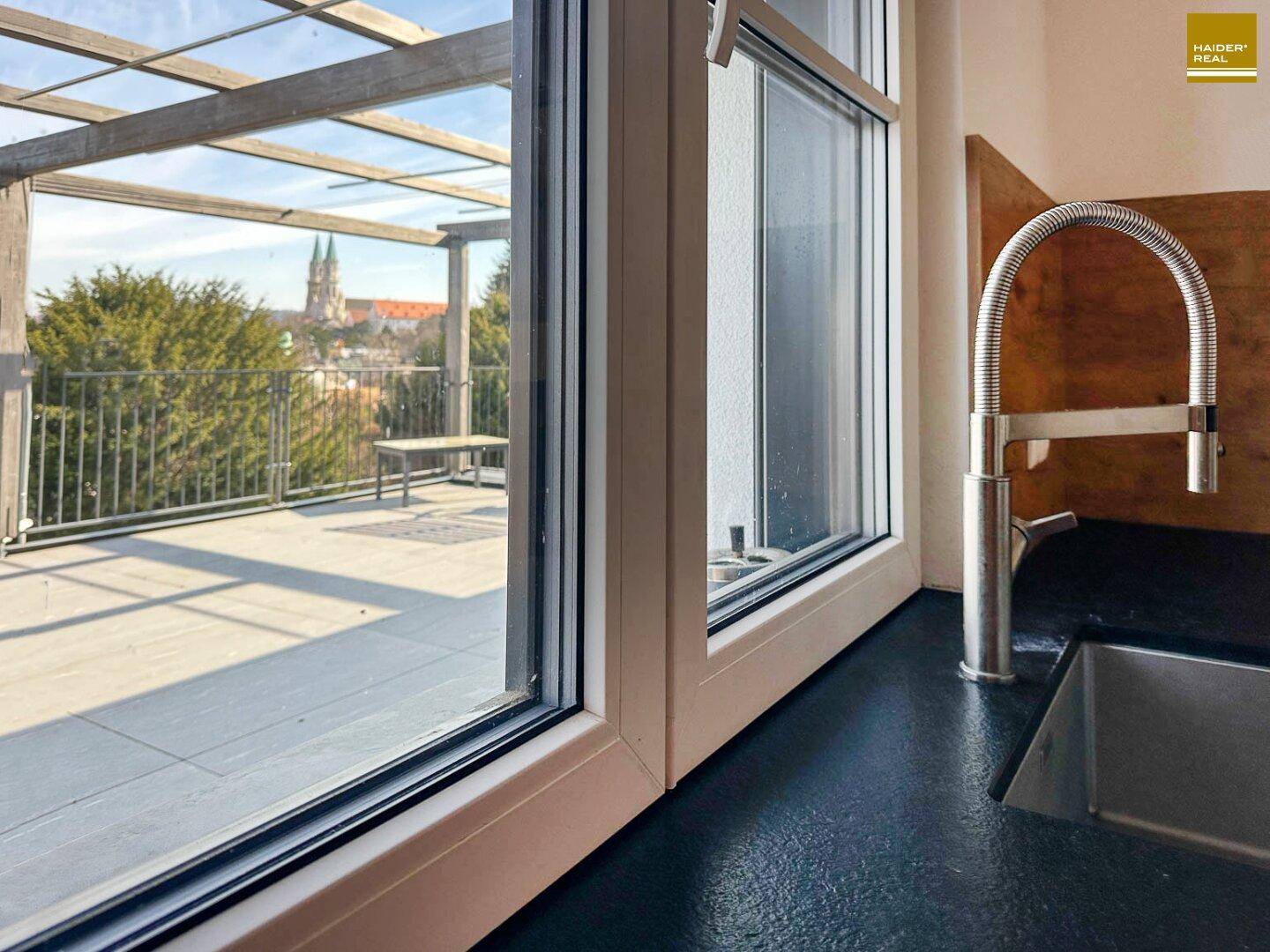 Küchenfenster mit Blick auf die Dachterrasse und die umliegende Stadtlandschaft mit Kirchturm.