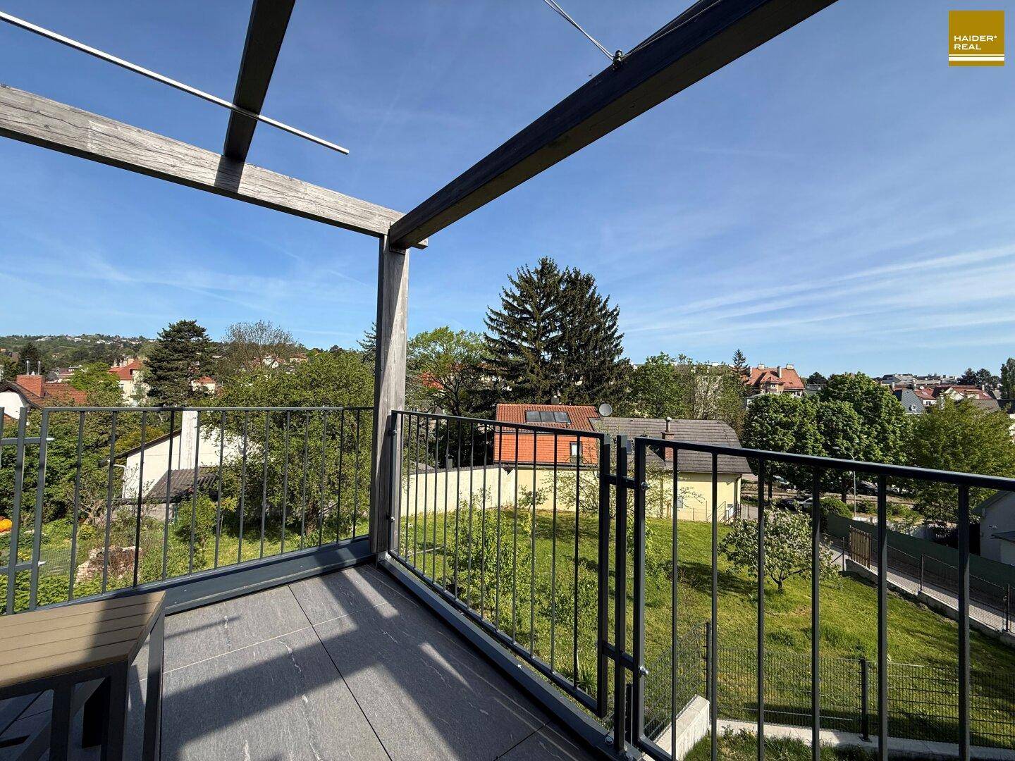 Balkon mit Metallgeländer und weitem Blick über grüne Gärten und die umliegende Wohngegend.