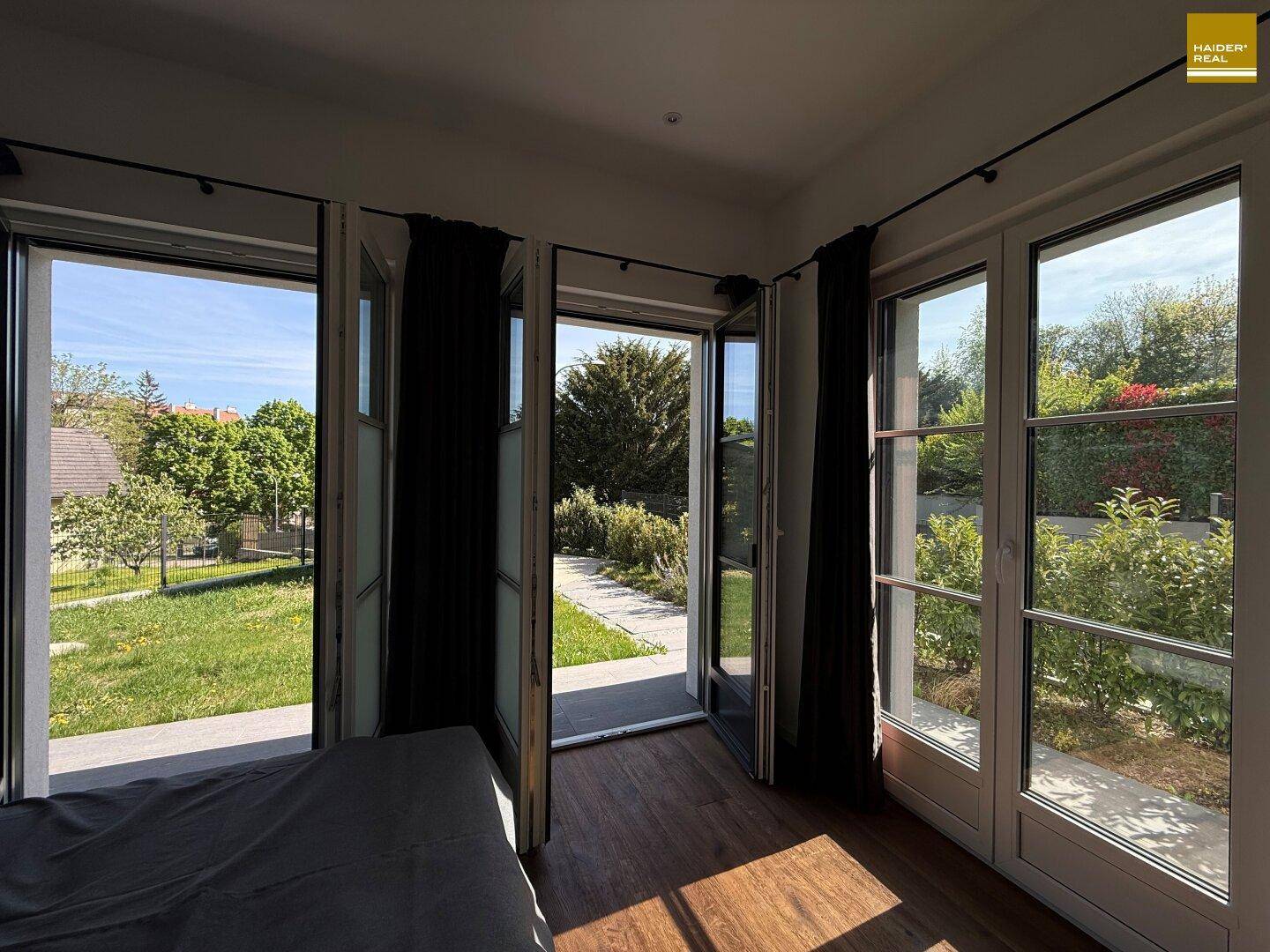 Schlafzimmer mit großen Fenstertüren, die direkten Zugang zum Garten und viel Tageslicht bieten.
