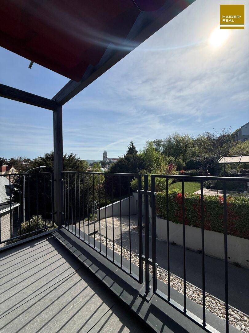 Balkon mit Metallgeländer und sonnigem Ausblick auf die Stadt und die grüne Umgebung.