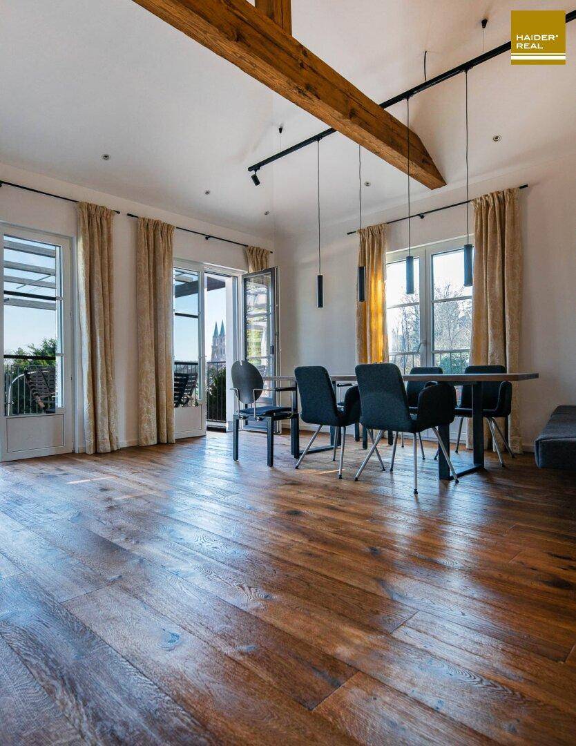 Geräumiger Wohn- und Essbereich mit Holzboden, sichtbaren Balken und Zugang zur Dachterrasse.