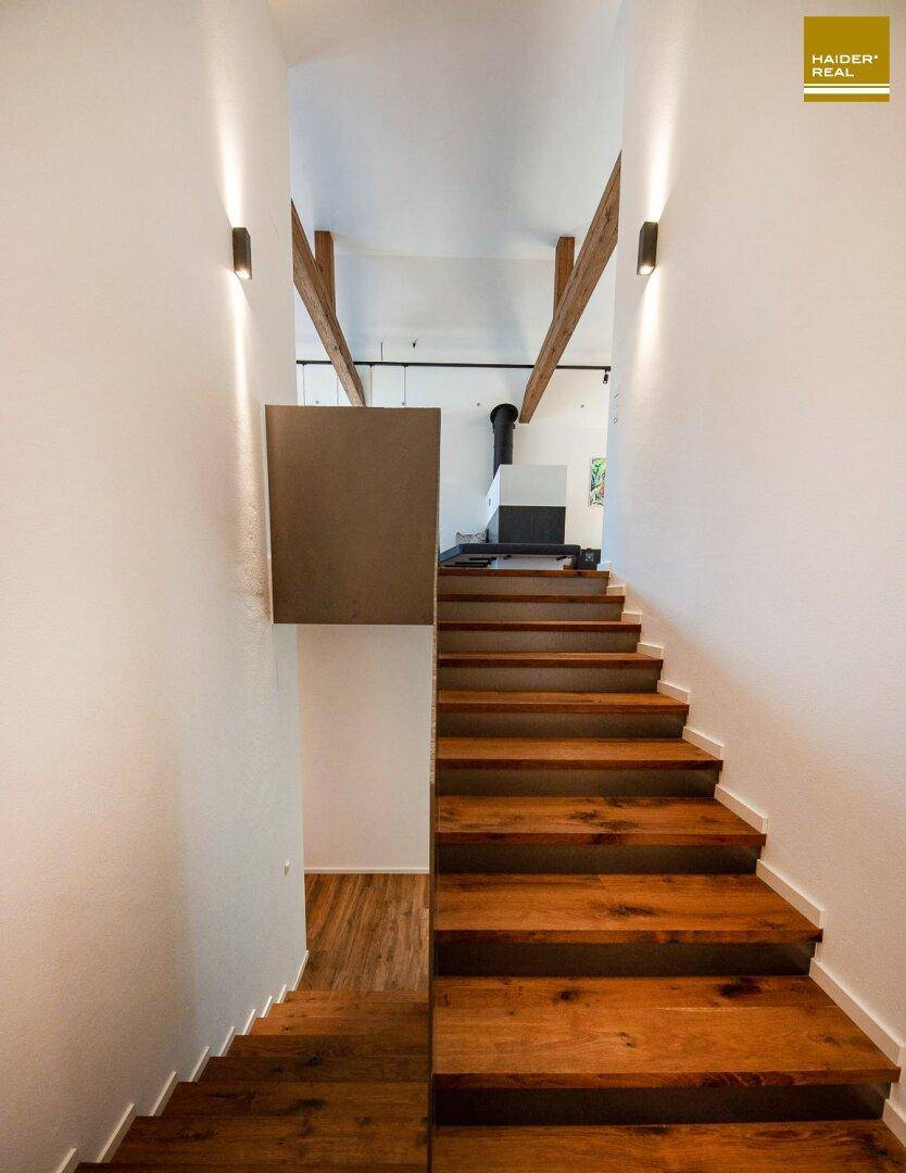 Elegante Holztreppe mit modernen Wandleuchten, die die verschiedenen Ebenen des Hauses verbindet.