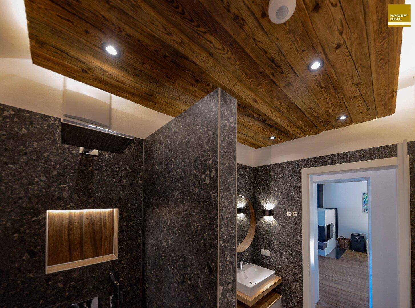 Modernes Badezimmer mit dunklen Fliesen, begehbarer Dusche und Holzdecke mit Einbaustrahlern.