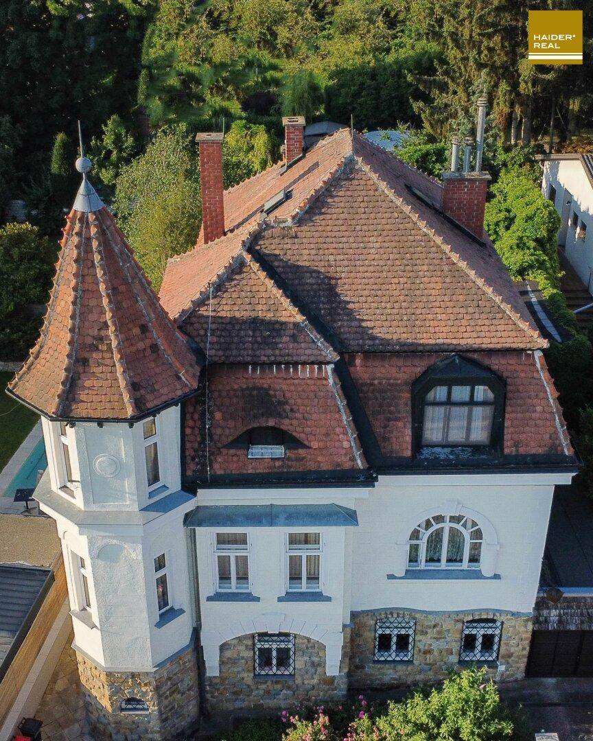 Luftaufnahme der historischen Villa mit Turm, Ziegeldach und umgebendem Grün.