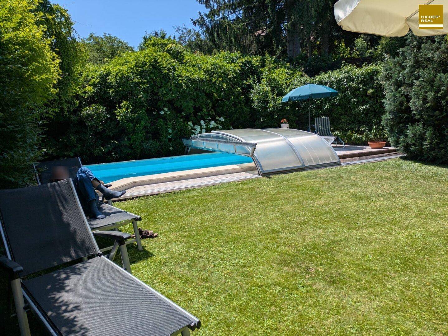 Gepflegter Gartenbereich mit Pool und Liegestühlen, umgeben von üppigem Grün.