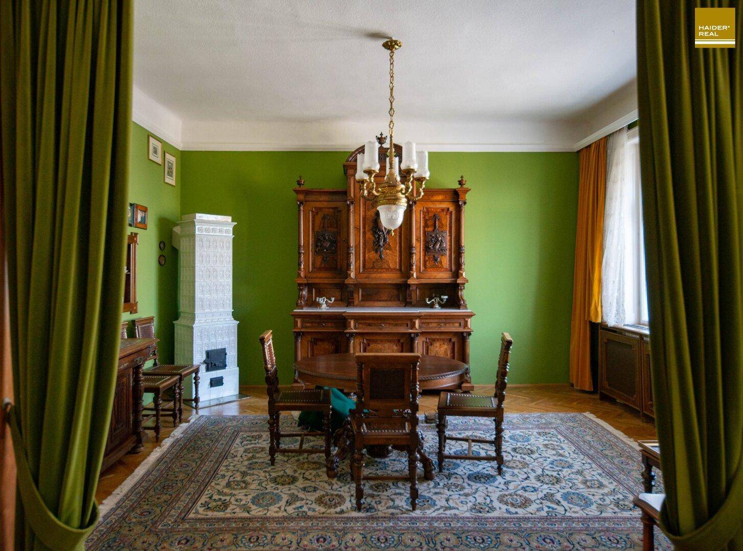 Elegantes Esszimmer mit grün gestrichenen Wänden, Kachelofen und antiken Holzmöbeln.