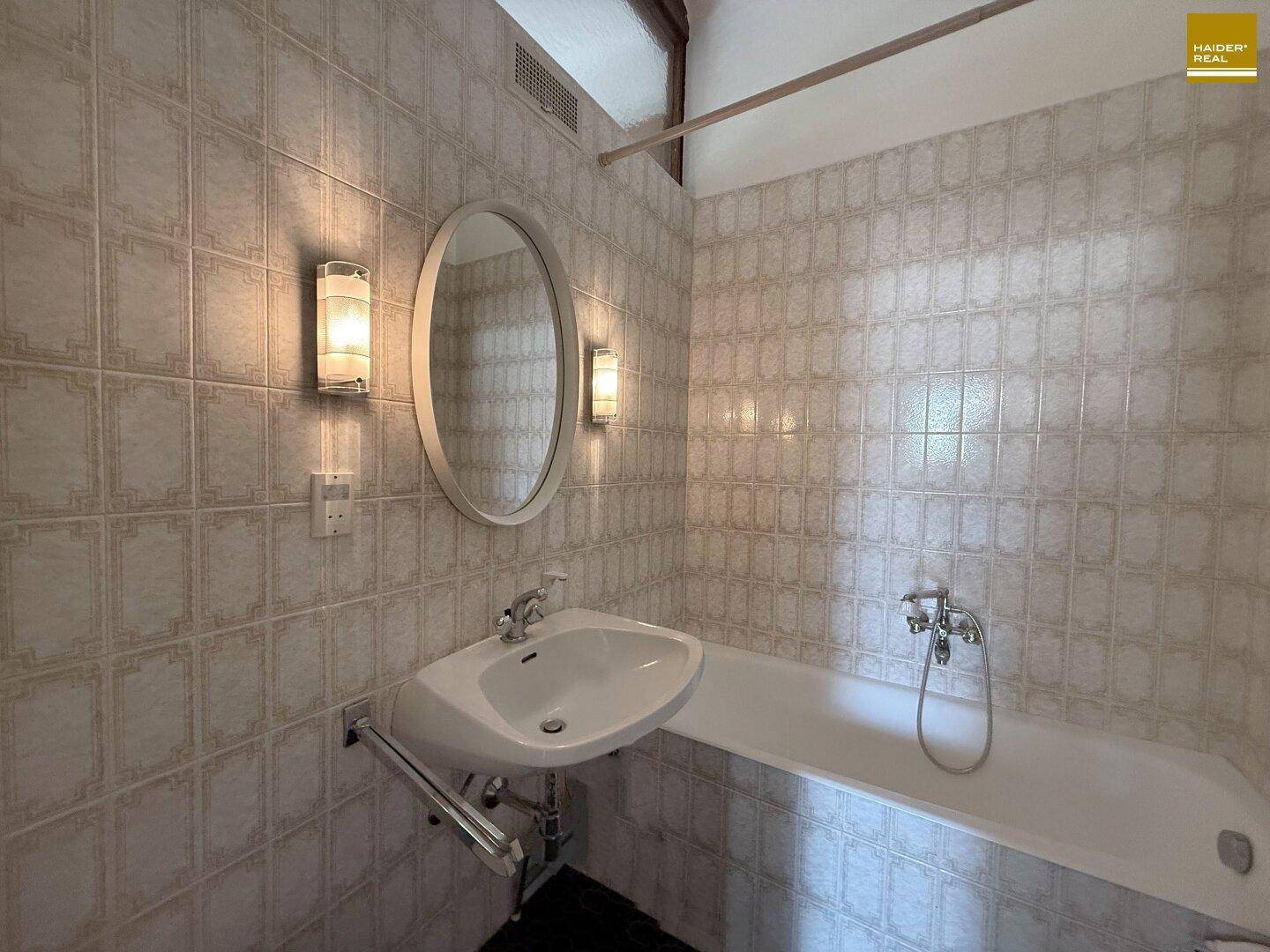 Badezimmer mit Badewanne, Waschbecken und hellen Fliesen an Wänden und Boden.