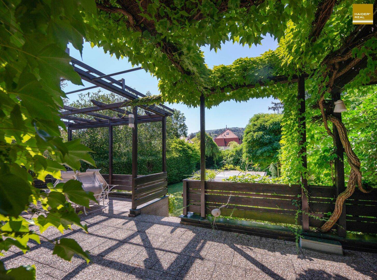 Überdachte Terrasse unter einer begrünten Pergola mit Gartenmöbeln und Weitblick.