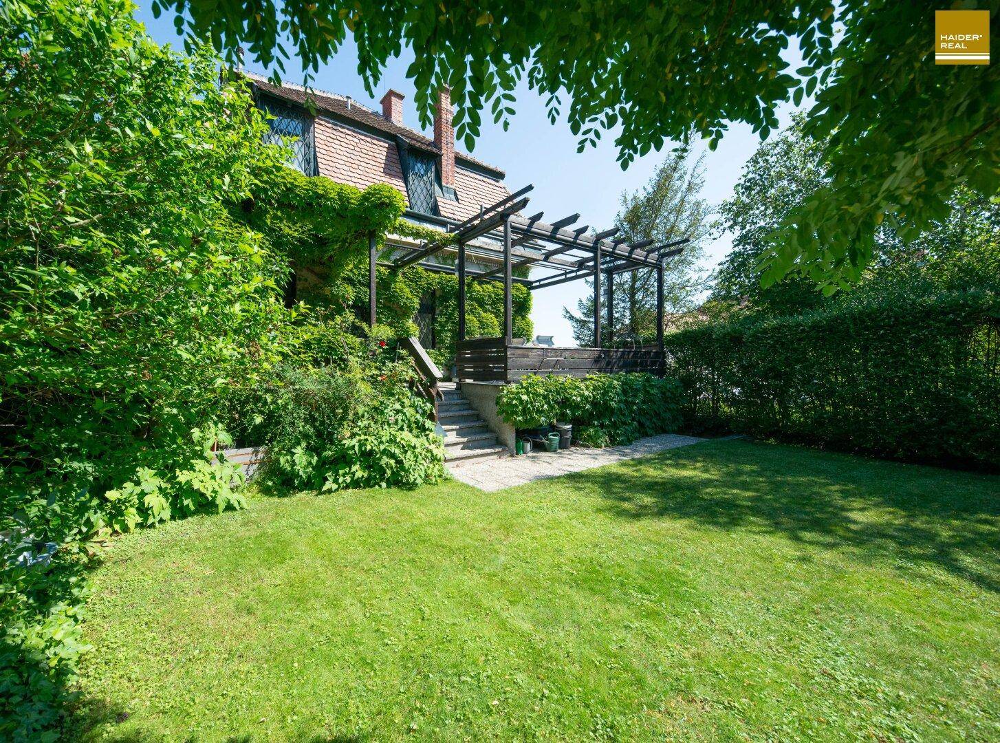Großer Garten mit Rasenfläche und einer charmanten Holzpergola, umgeben von Bäumen.