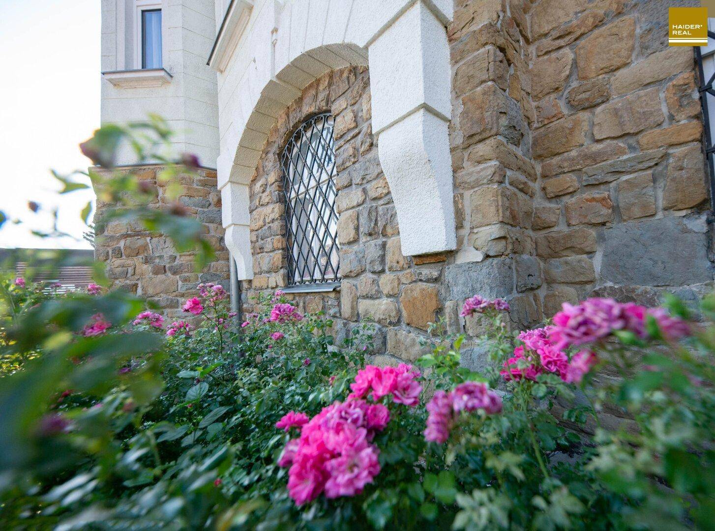 Nahaufnahme der Steinfassade mit blühenden Rosenbüschen im Vorgarten.
