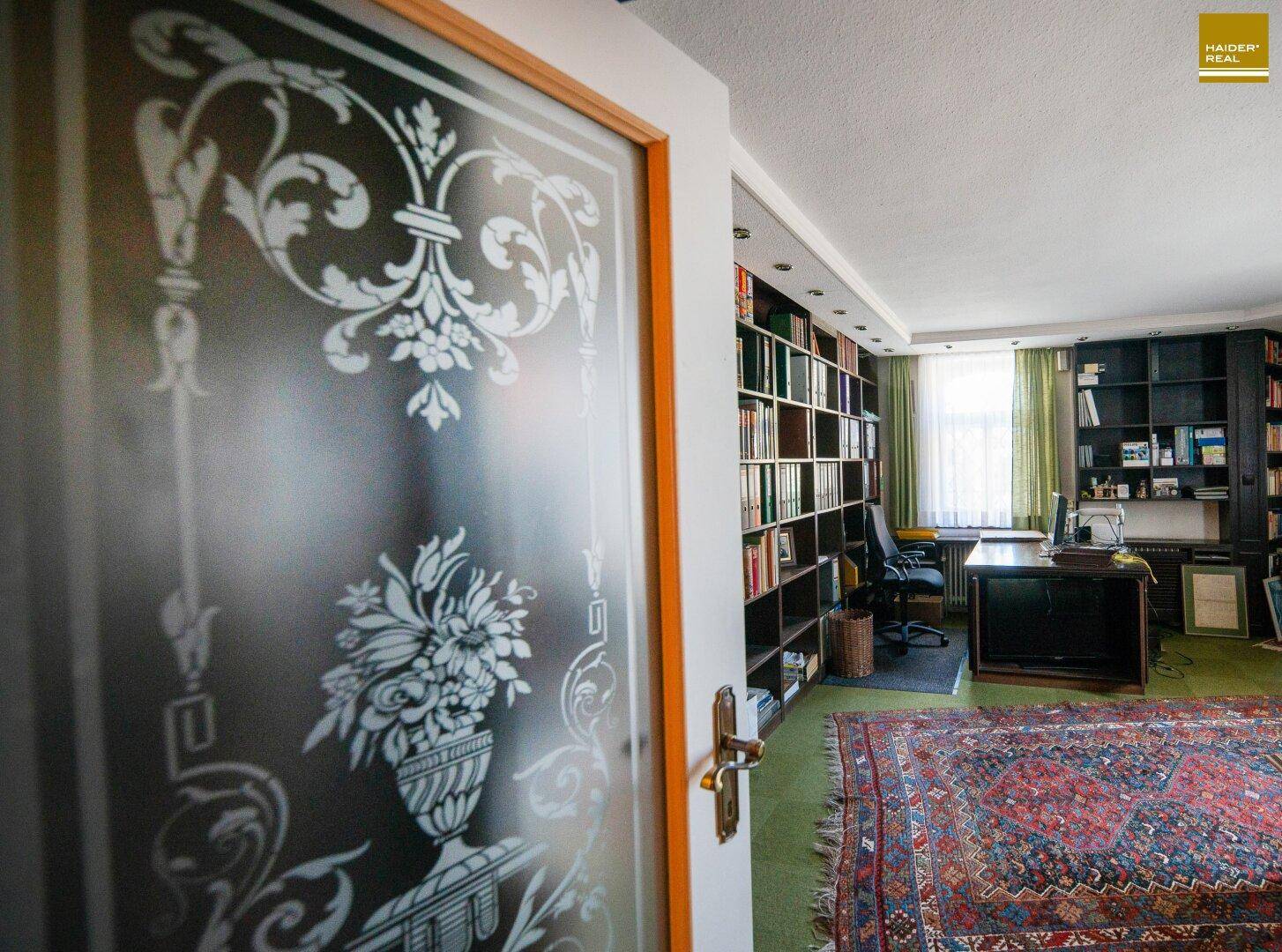 Großes Arbeitszimmer mit Bücherregalen, Schreibtisch und Teppichboden.