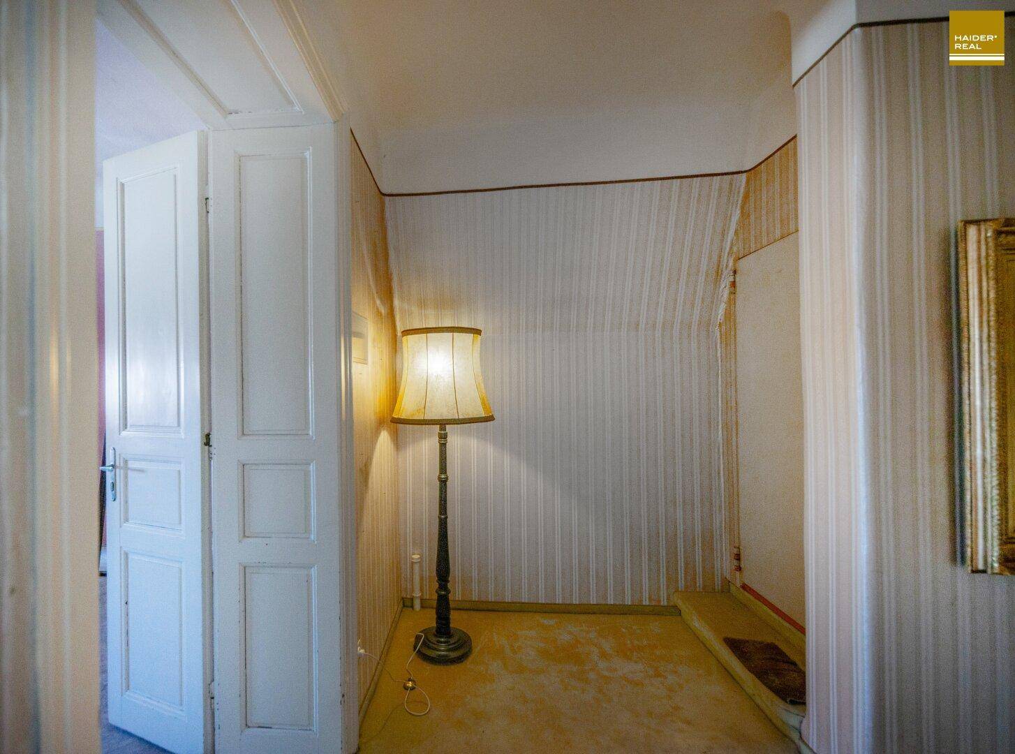 Heller Flurbereich mit gestreifter Tapete, Stehlampe und Zugang zu weiteren Räumen.