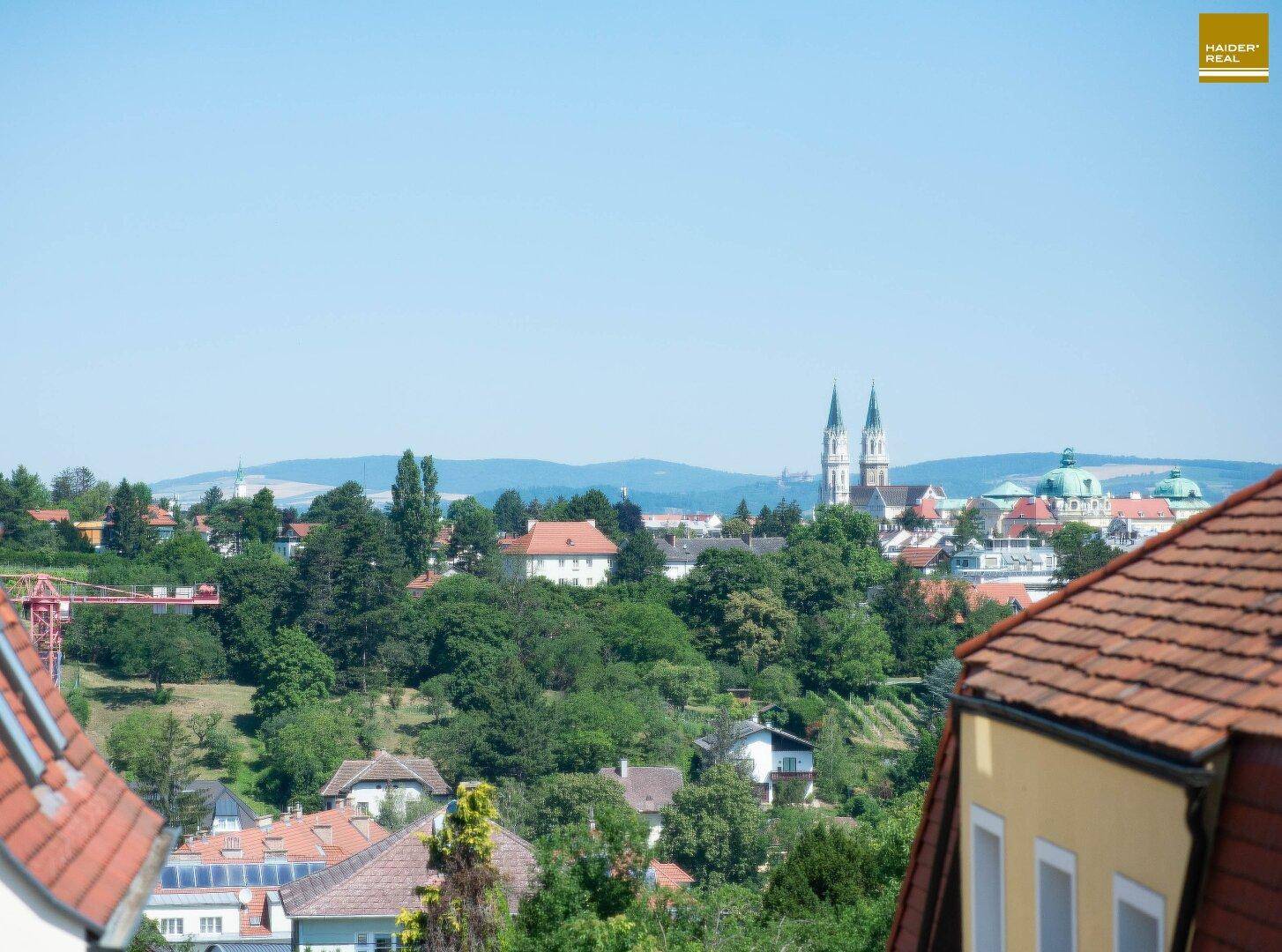 Panoramablick über die Stadt mit Kirchtürmen und grünen Hügeln im Hintergrund.
