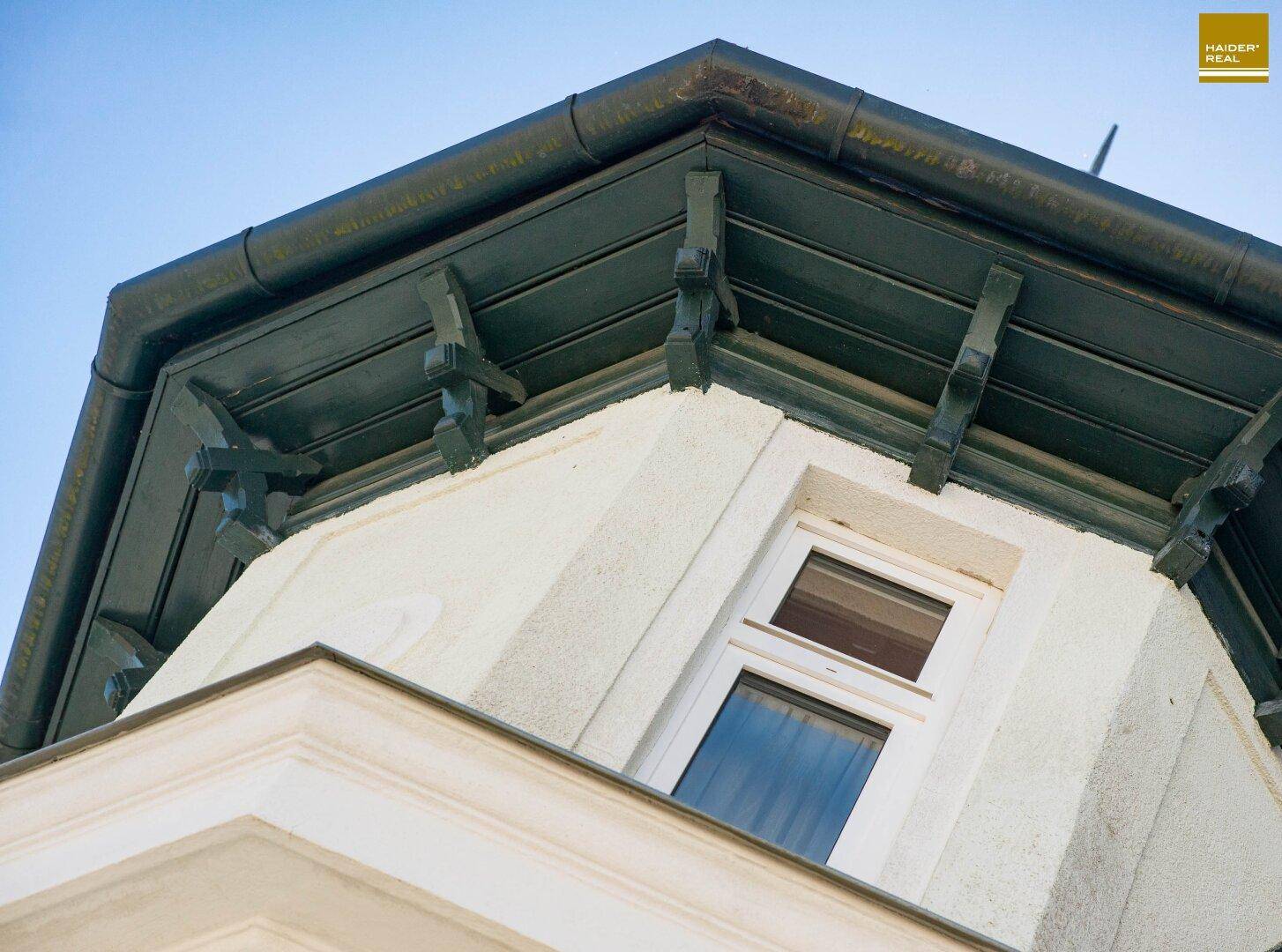 Detail des Daches mit verzierten Holzbalken und Regenrinne unter blauem Himmel.