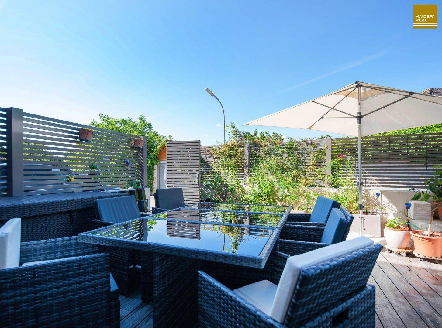 Gemütliche Terrasse mit Outdoor-Sitzgruppe und Sonnenschirm, umgeben von Pflanzen.