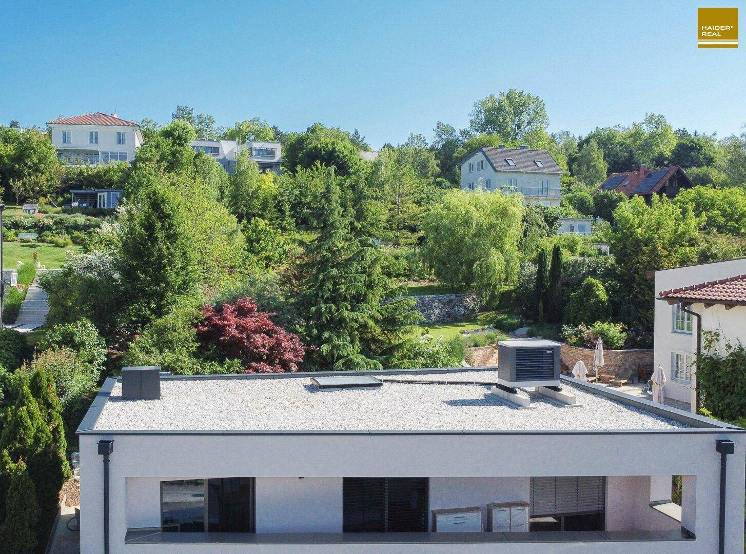 Panoramablick auf das moderne Haus mit Flachdach und die grüne, hügelige Wohngegend.