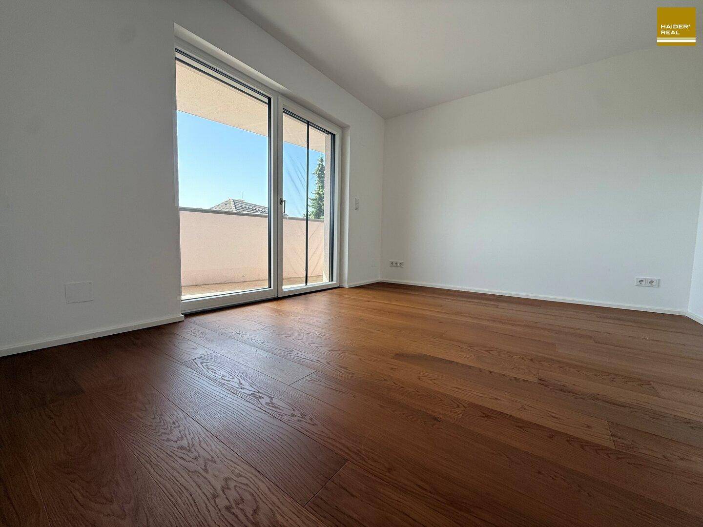 Geräumiges Schlafzimmer mit Holzboden und großen Schiebetüren zum Balkon.