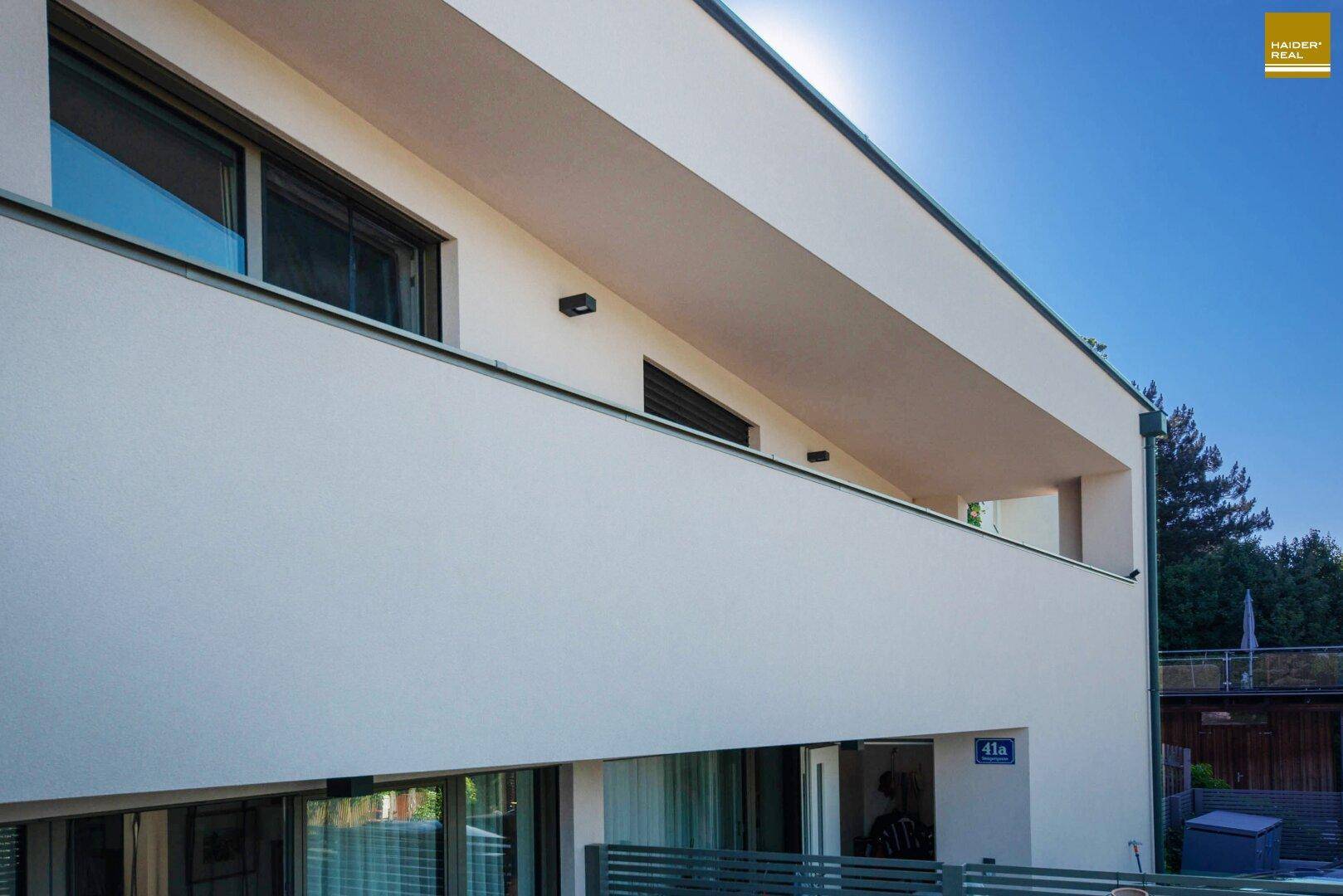 Detailansicht der modernen Hausfassade mit Balkon und großen Fenstern unter blauem Himmel.