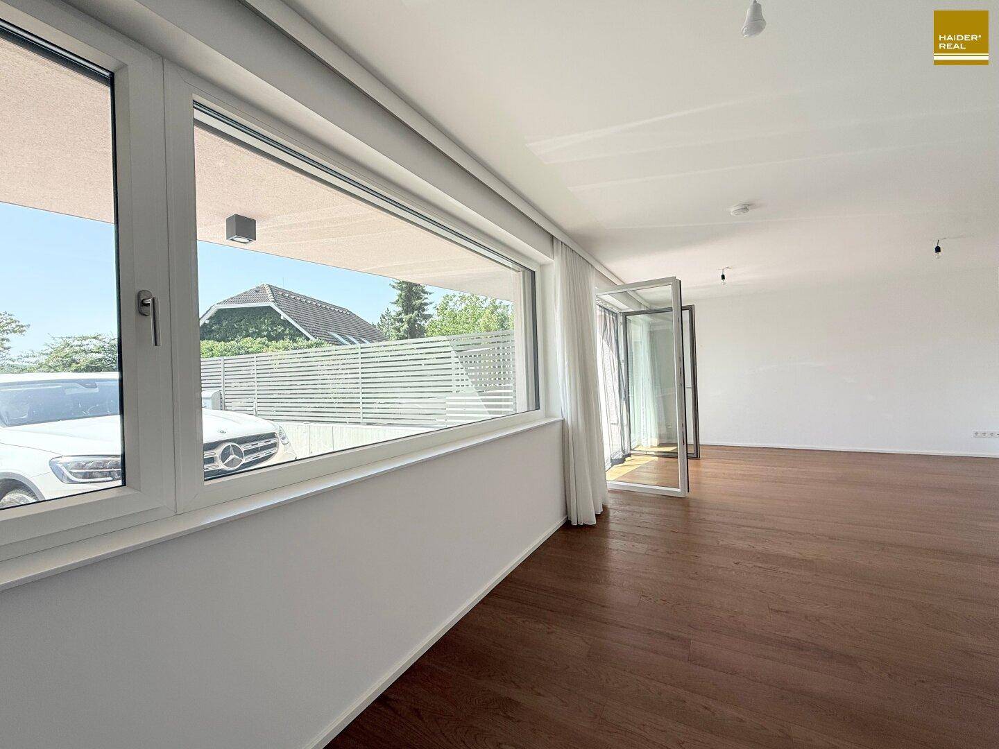 Heller Wohnraum mit Holzboden und großen Fenstern, die viel Tageslicht hereinlassen.