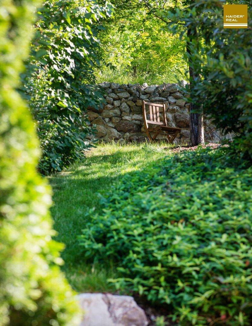 Ruhiger Gartenbereich mit einem Holzstuhl und einer Natursteinmauer im Hintergrund.