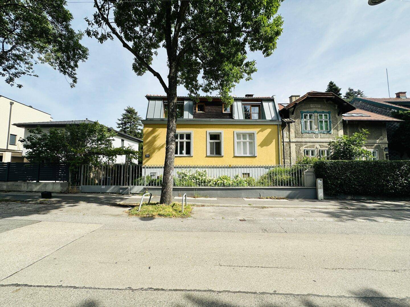 Gelbe Hausfassade mit mehreren Fenstern und einem Mansarddach, sichtbar von der Straße.