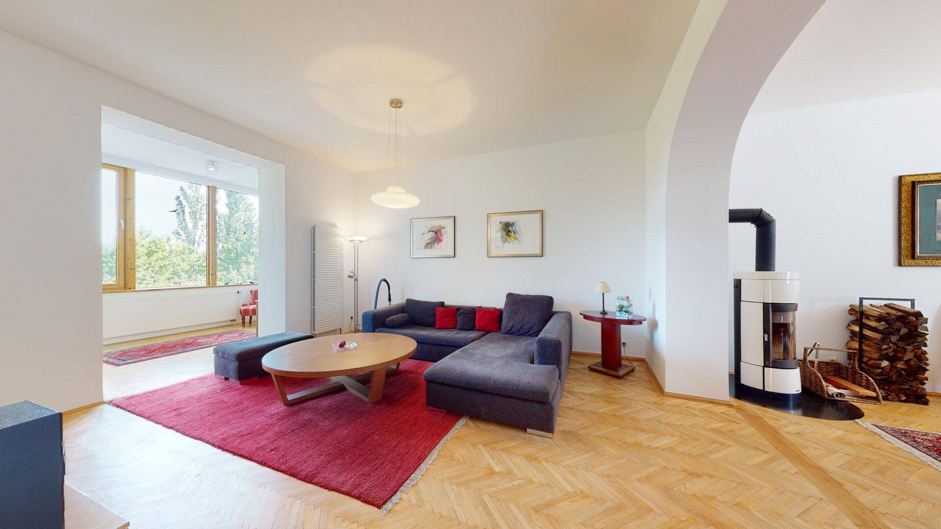 Geräumiges Wohnzimmer mit Fischgrätparkett, modernem Kaminofen und großen Fenstern.