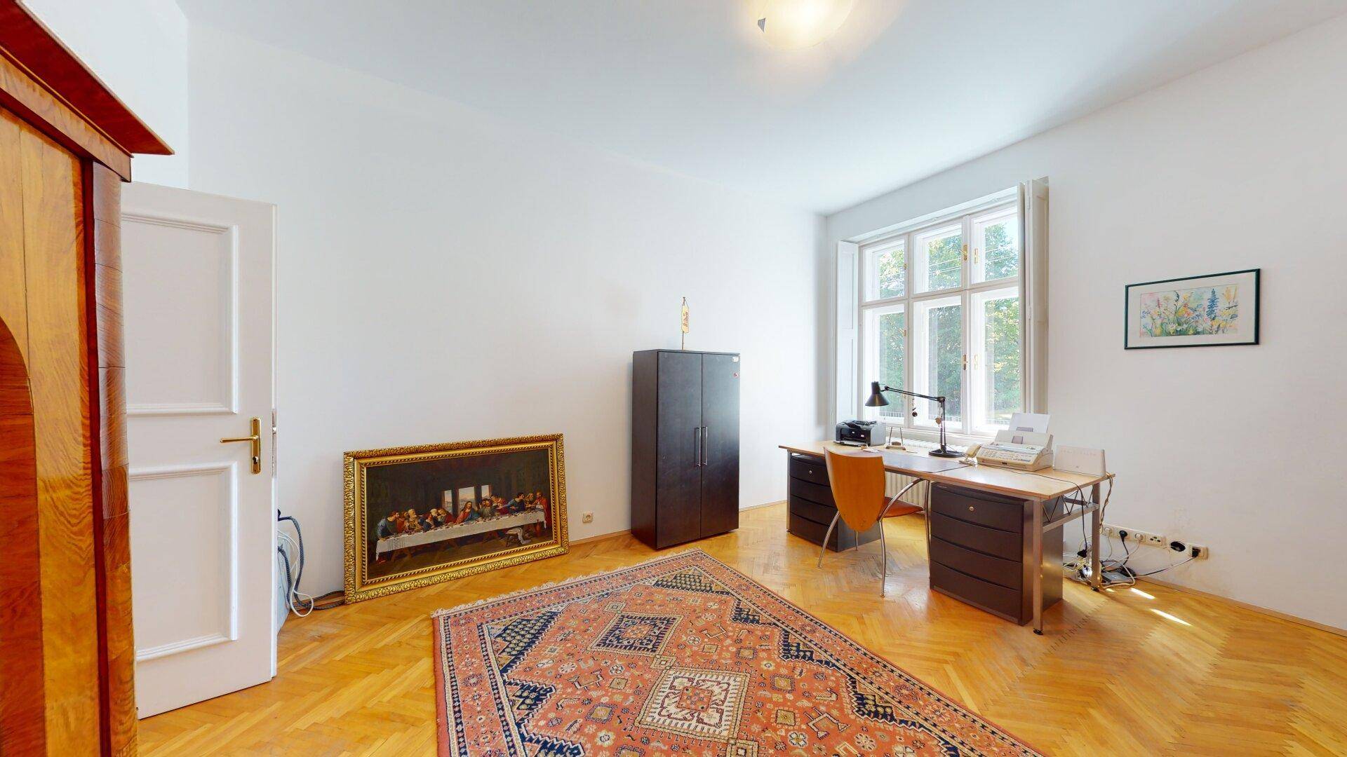 Helles Arbeitszimmer mit Parkettboden, großem Fenster und einem Schreibtisch mit Bürostuhl.