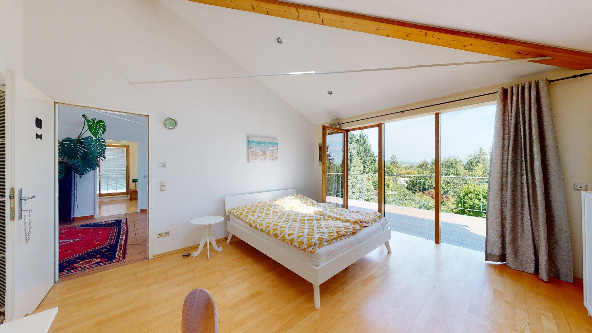 Helles Schlafzimmer mit Holzboden, hohen Decken und direktem Zugang zu einem Balkon mit Aussicht.