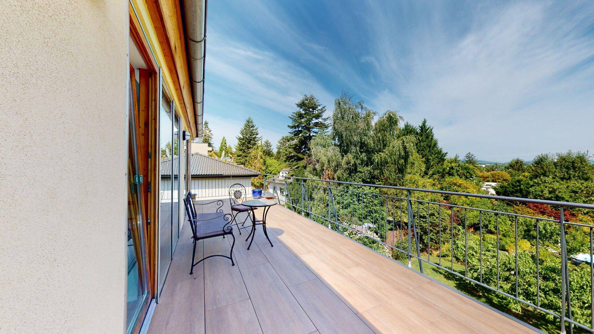 Geräumiger Balkon mit Holzboden, Sitzgelegenheiten und weitem Blick über die grüne Umgebung.