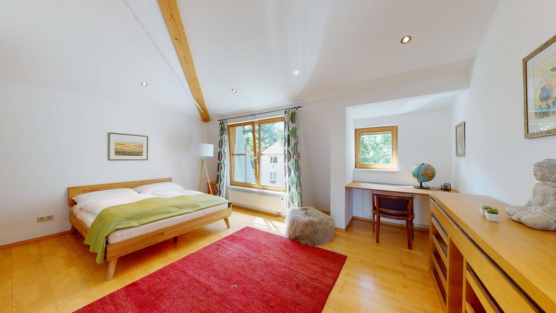 Gemütliches Schlafzimmer mit Holzboden, Holzbalken und einem integrierten Arbeitsbereich am Fenster.