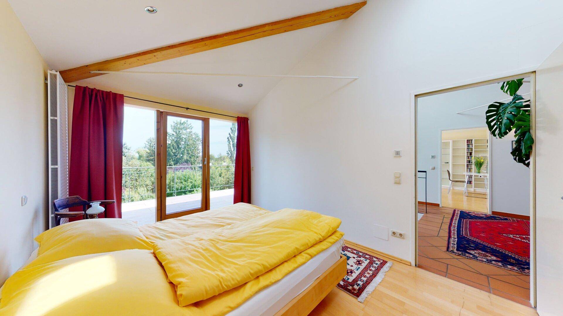 Helles Schlafzimmer mit Holzboden, hohen Decken und direktem Zugang zu einem Balkon.