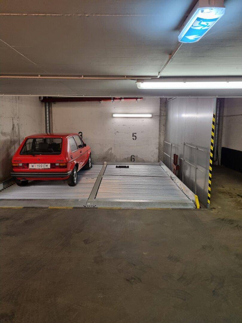 Tiefgaragenstellplatz mit mechanischem Parksystem und einem roten Auto, beleuchtet von Leuchtstoffröhren.