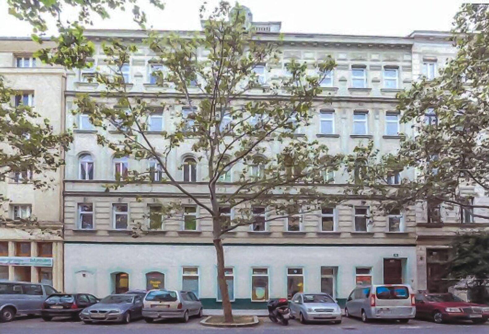 Historische Gebäudefassade mit vielen Fenstern und parkenden Autos auf der Straße.