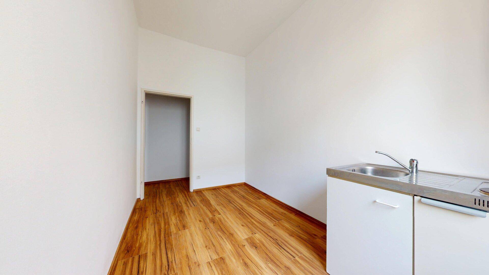 Leerer Küchenbereich mit Spüle und Unterschrank, Laminatboden und Türzugang.