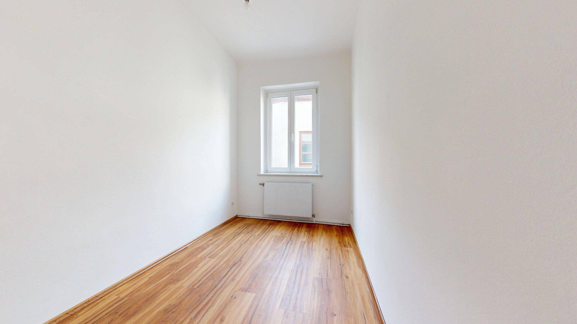 Kleiner, heller Raum mit Laminatboden und Fenster, ideal als Schlaf- oder Arbeitszimmer.