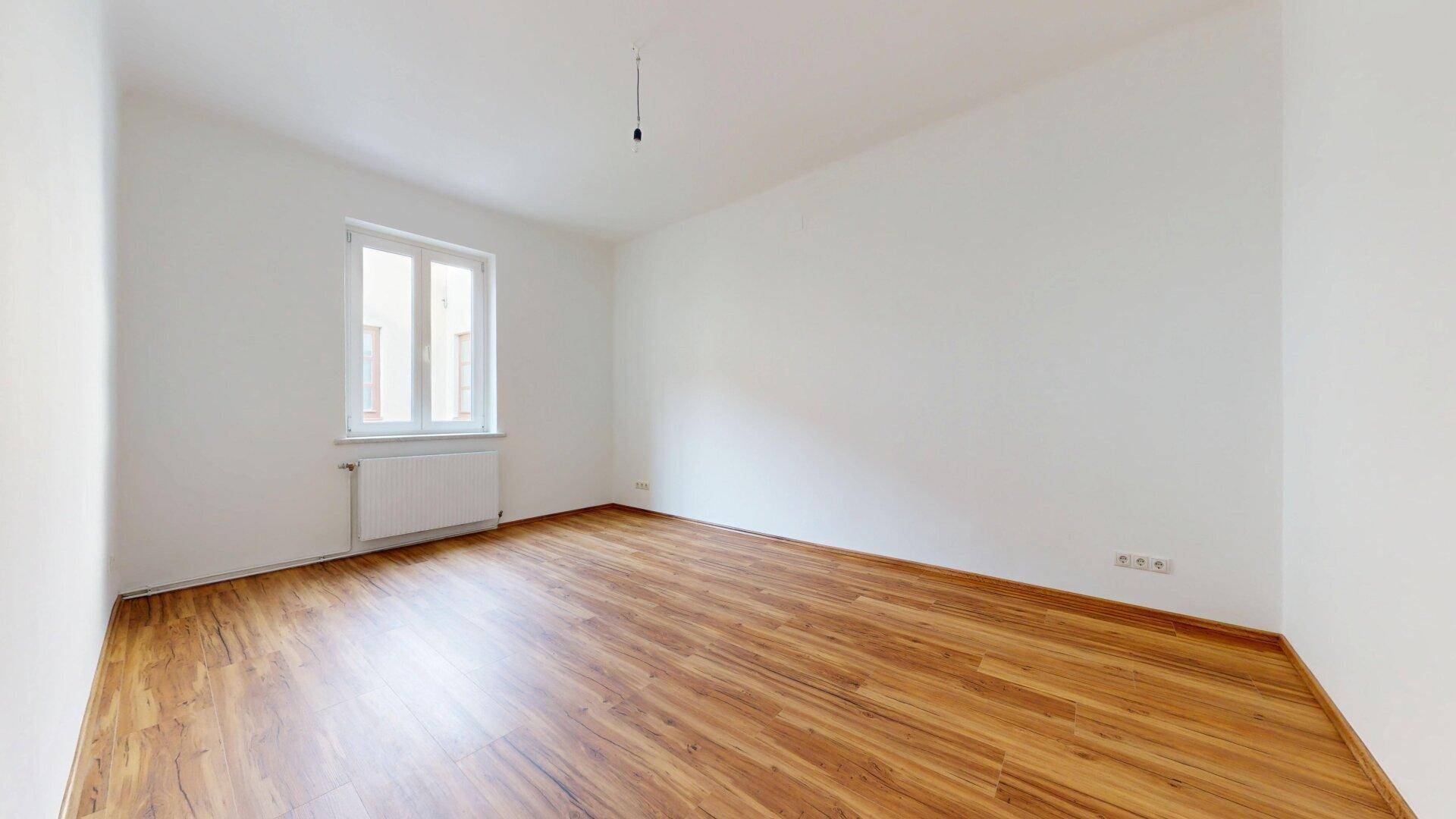 Heller, leerer Raum mit Laminatboden und einem Fenster, bereit zur individuellen Gestaltung.