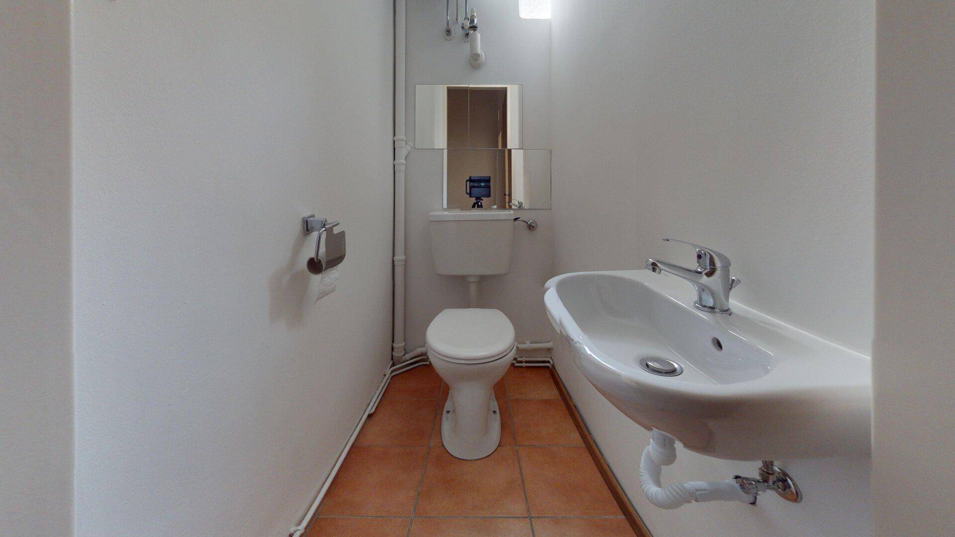 Einfache Toilette mit Waschbecken und Terrakotta-Fliesenboden, funktional und sauber.