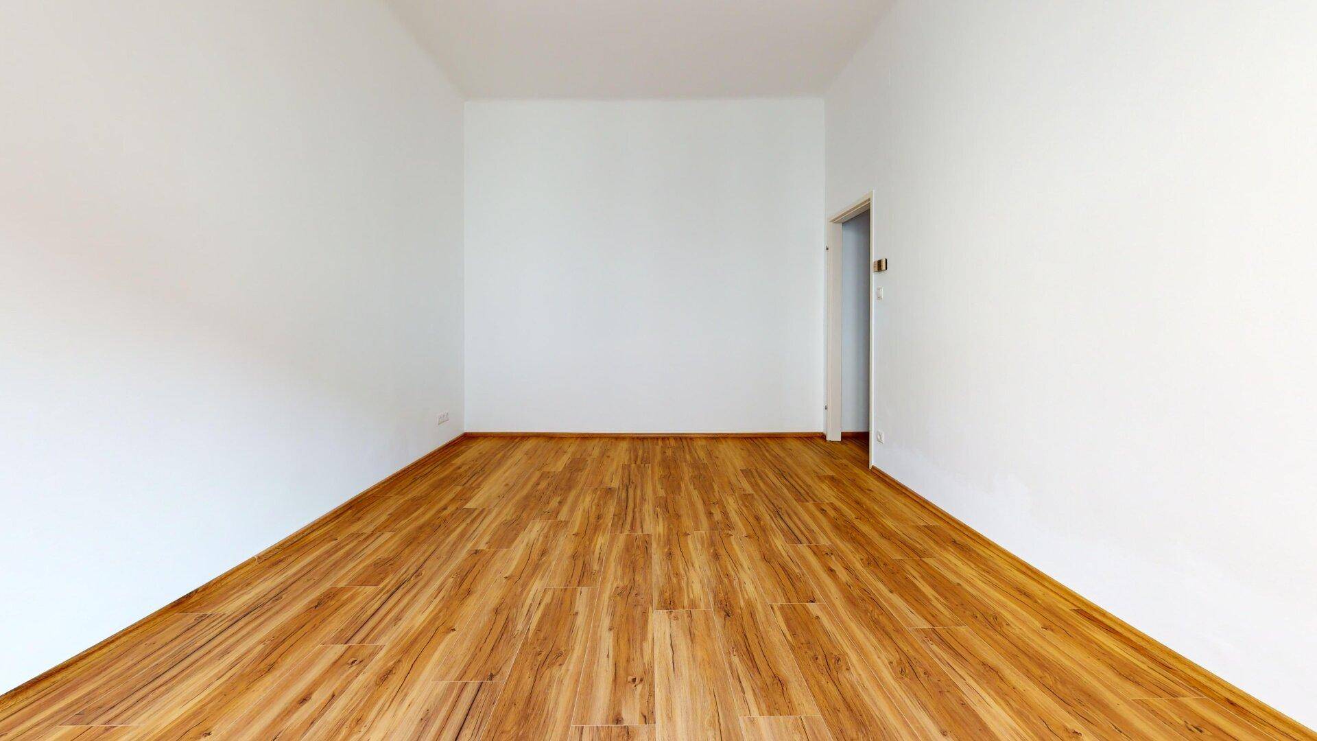 Langer, schmaler Raum mit Laminatboden und weiß gestrichenen Wänden, mit Türzugang.