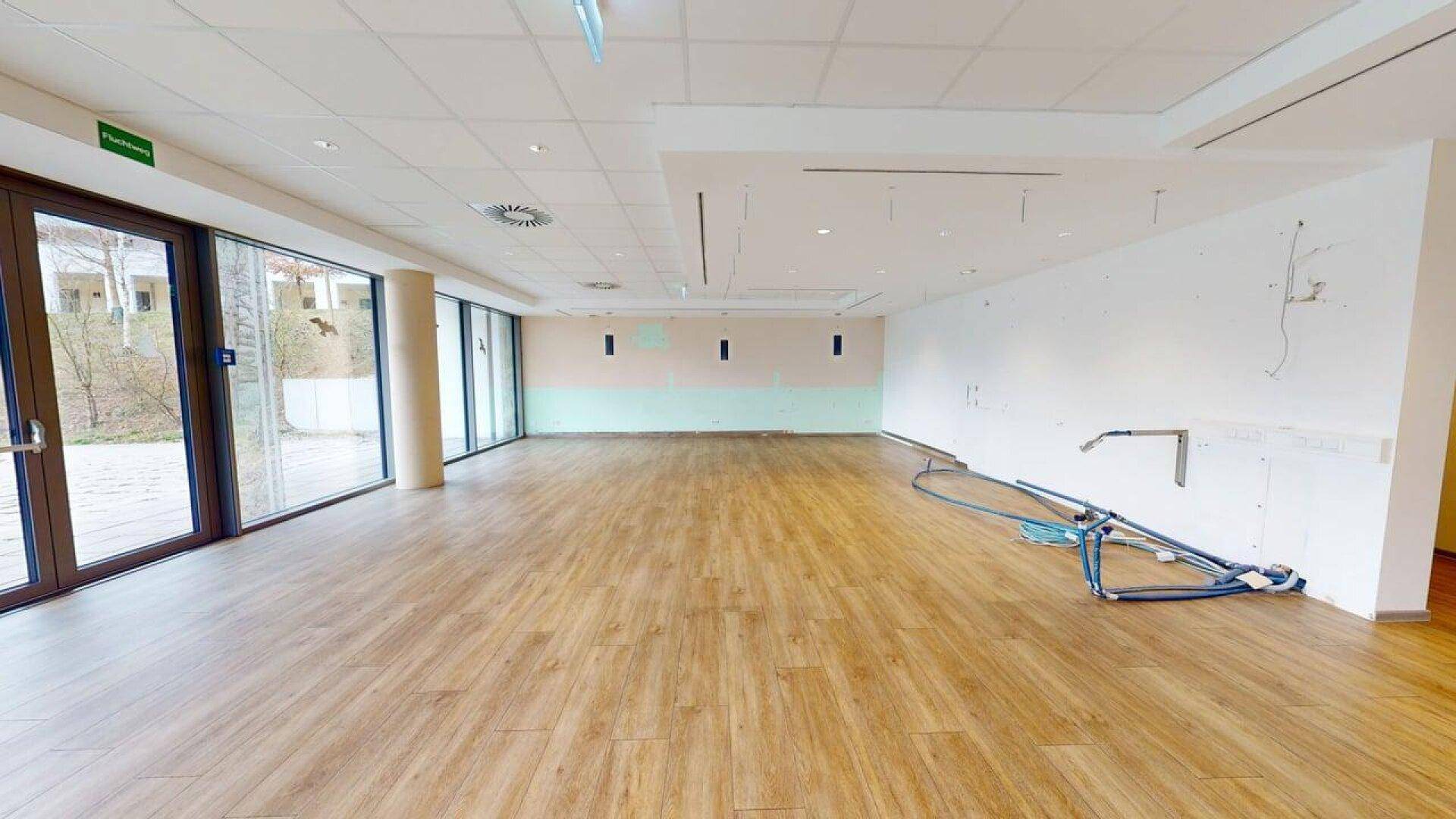 Heller Gewerberaum mit Laminatboden und großen Fenstern, teilweise mit Wandvorbereitungen für Installationen.