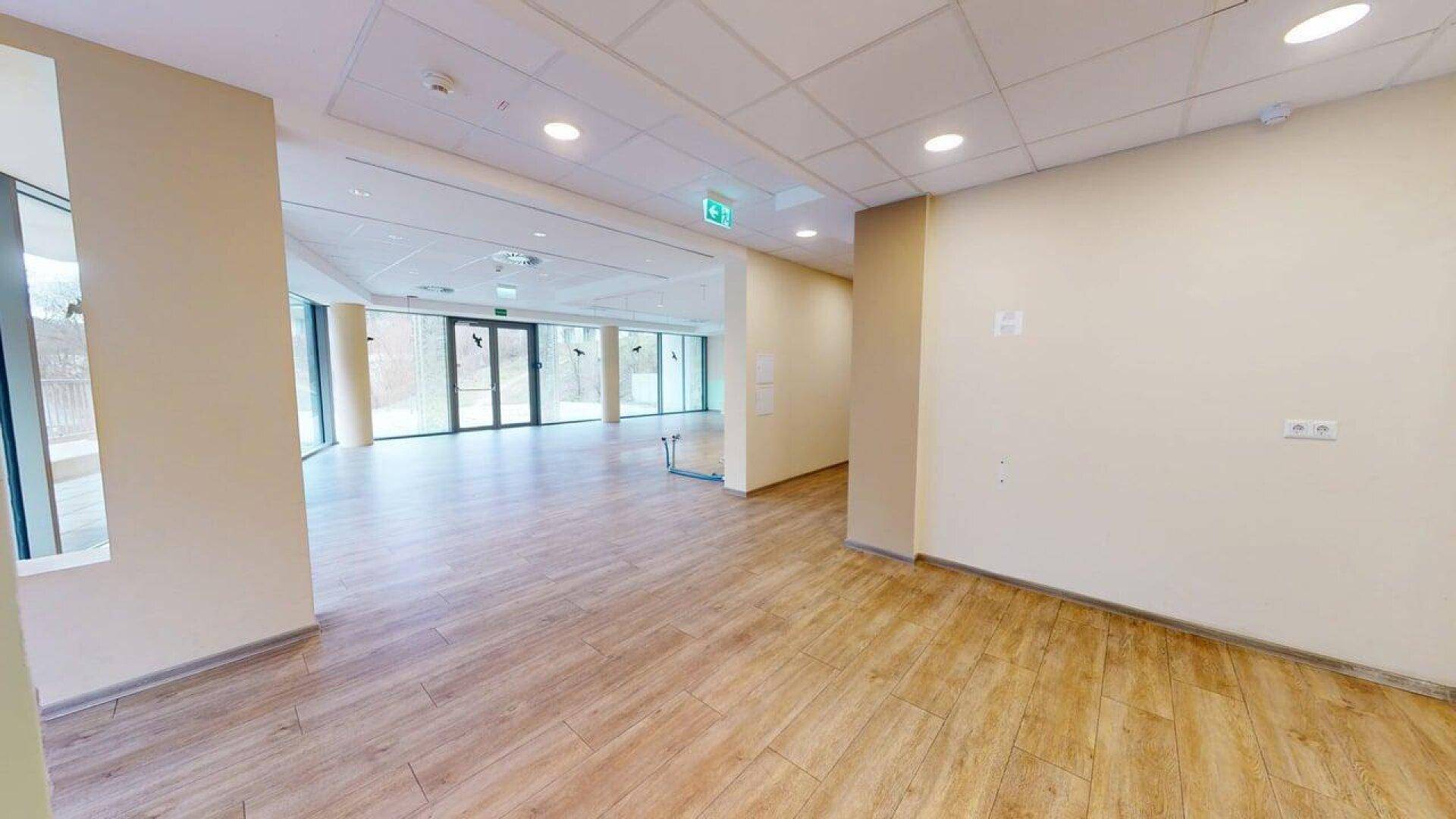 Langer, heller Gewerberaum mit Holzboden und großen Fenstern, der in einen weiteren Bereich führt.