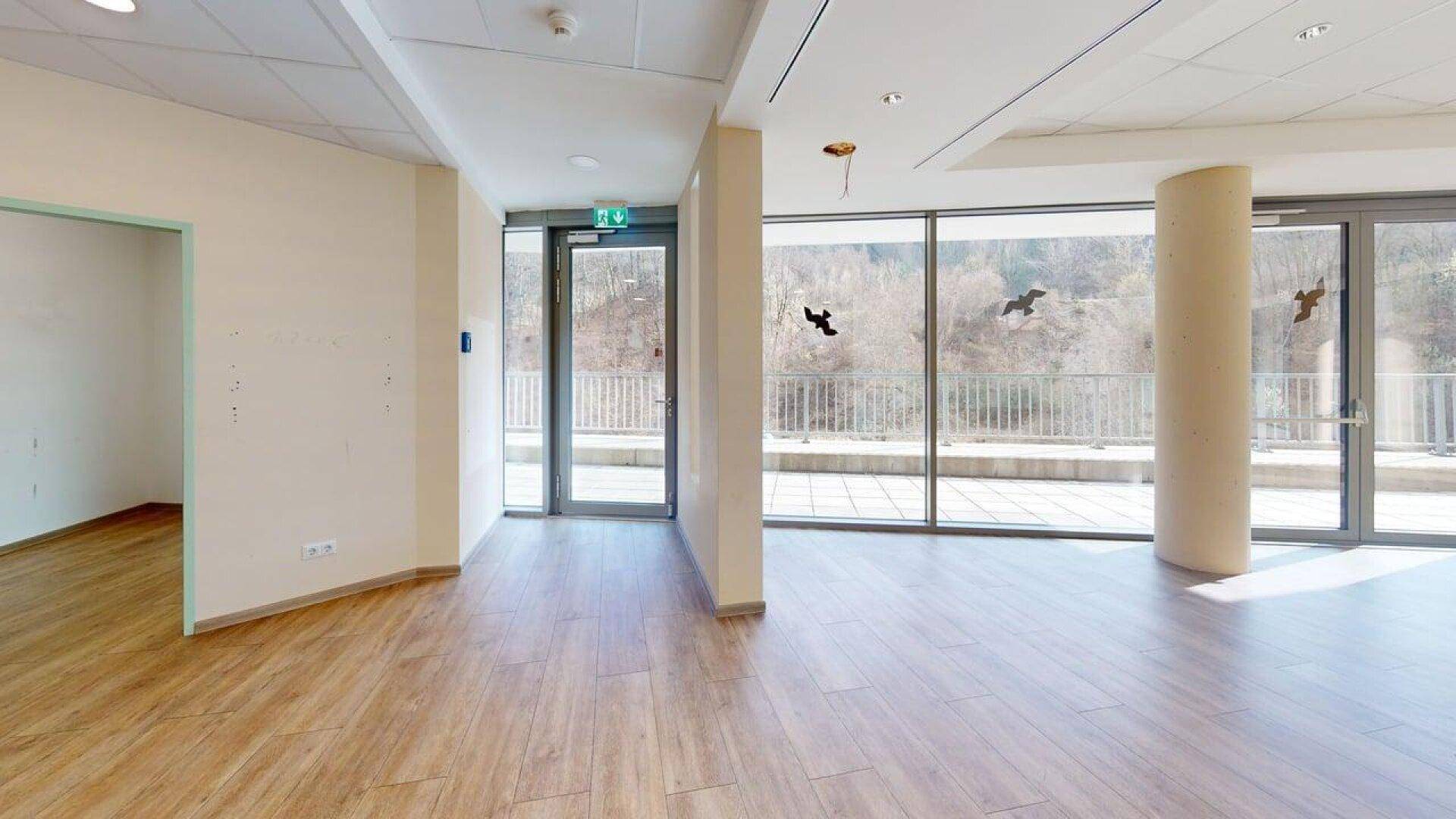 Großer, heller Gewerberaum mit Laminatboden und bodentiefen Fenstern, die auf eine Terrasse führen.