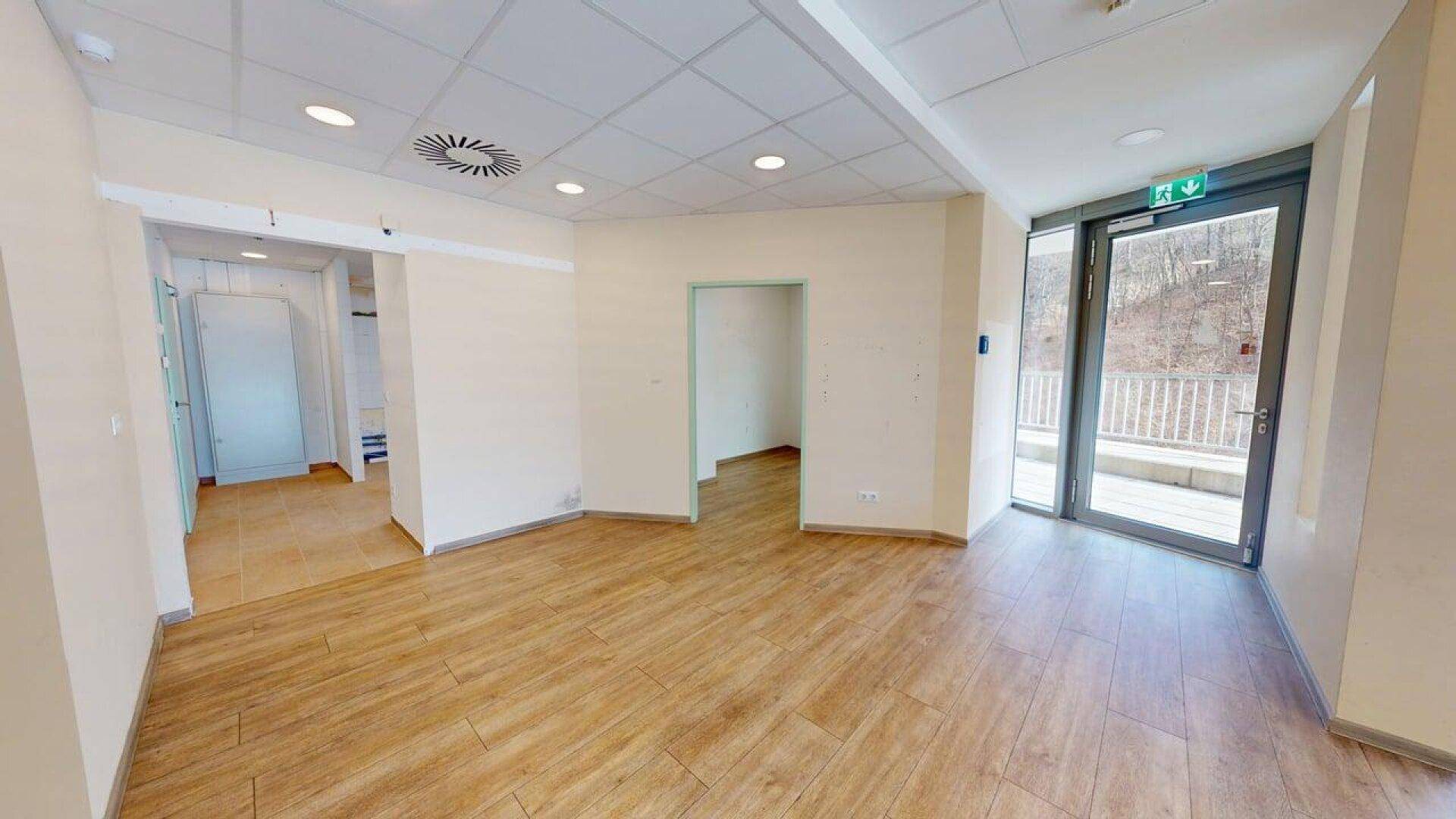 Heller Gewerberaum mit Laminatboden, der zu mehreren kleineren Räumen und einem Ausgang führt.