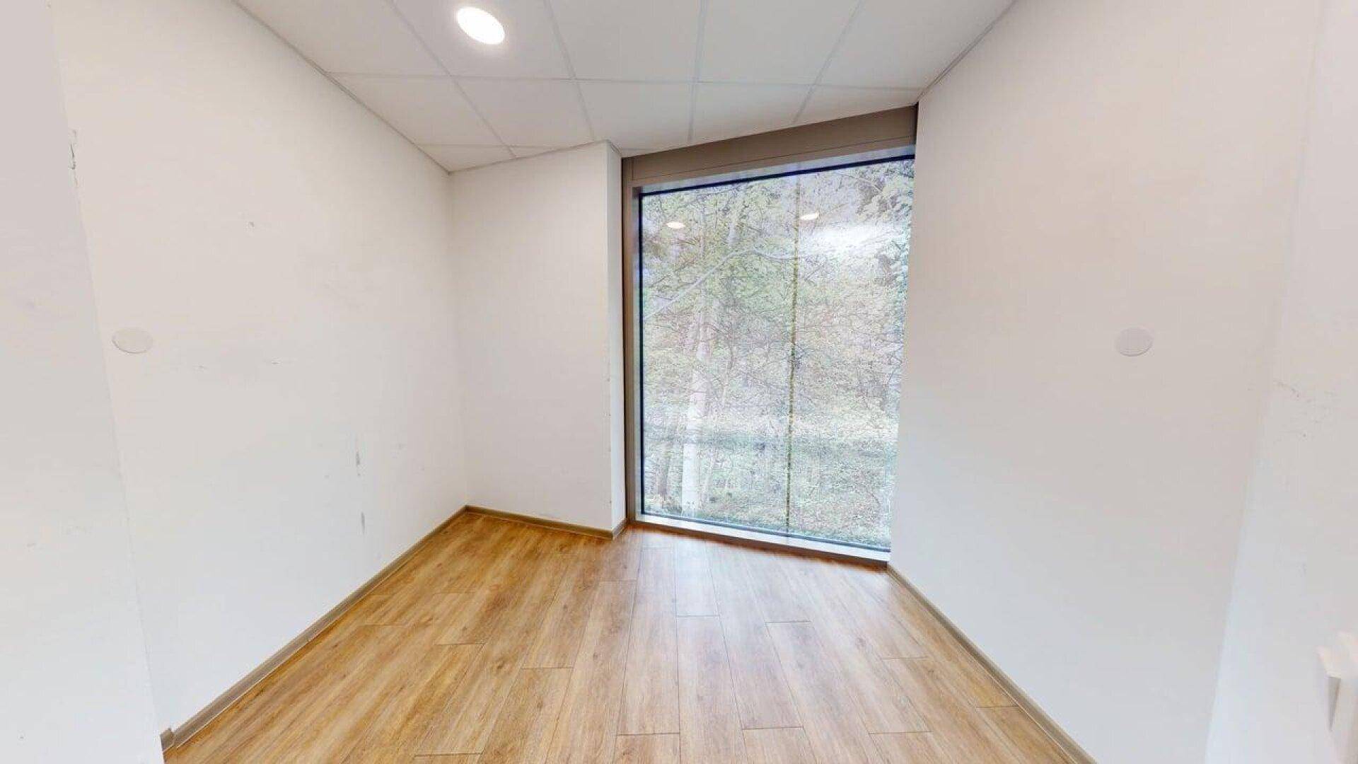 Kleiner, heller Büroraum mit Holzboden und einem großen Eckfenster, das viel Licht hereinlässt.