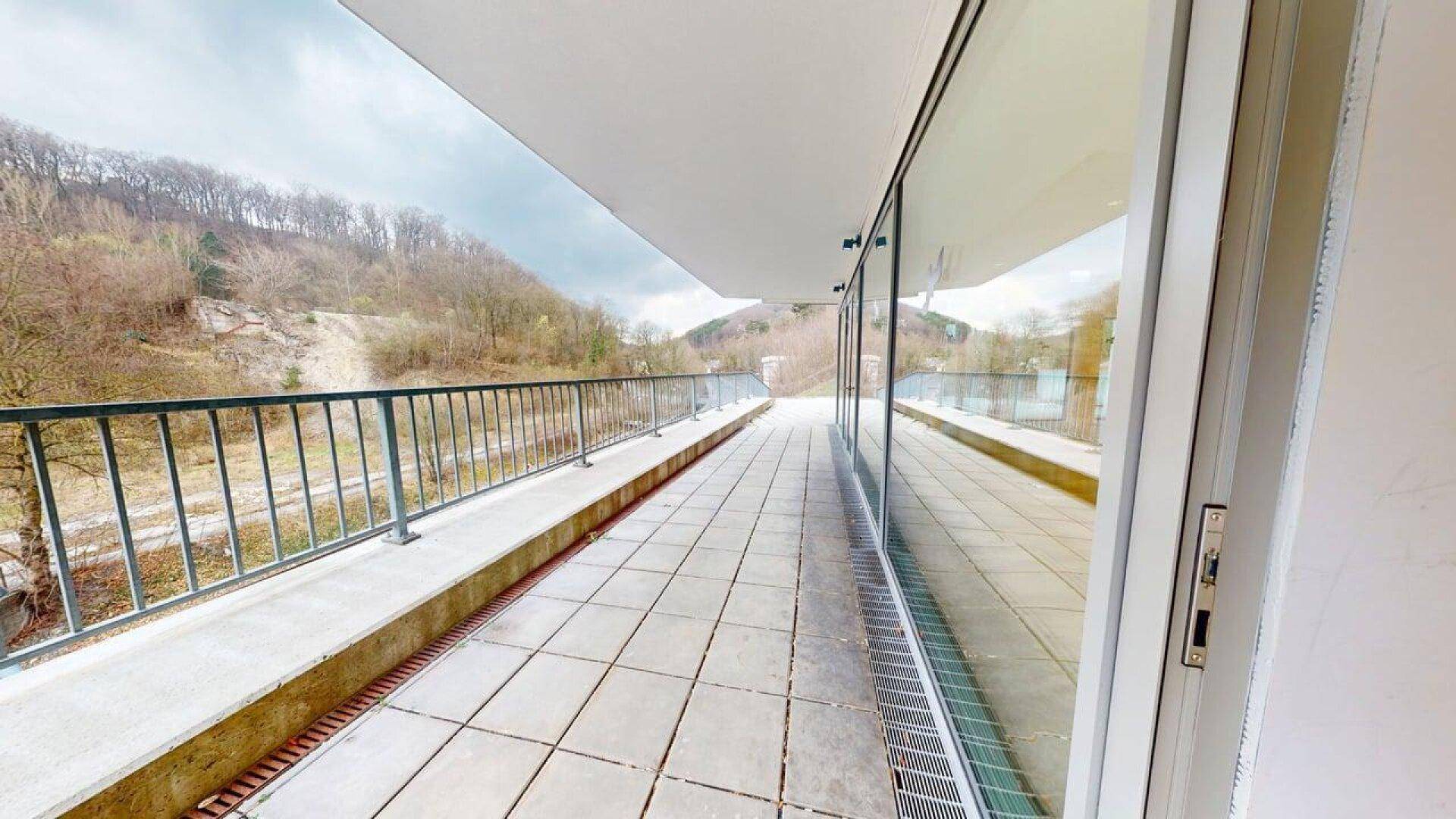 Lange, geflieste Terrasse mit Metallgeländer und Blick auf bewaldete Hügel, ideal für Entspannung.