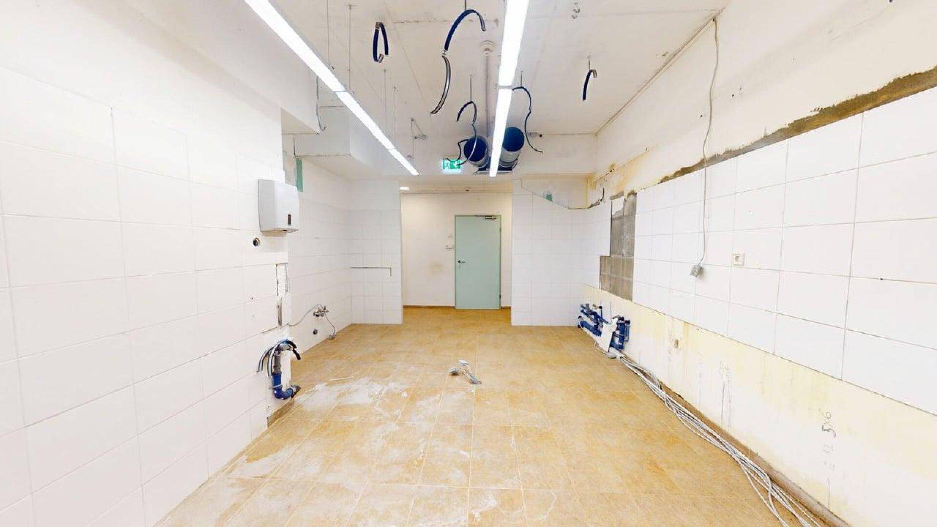 Unfertige Küche mit gefliesten Wänden und Boden, vorbereitet für die Installation von Geräten.