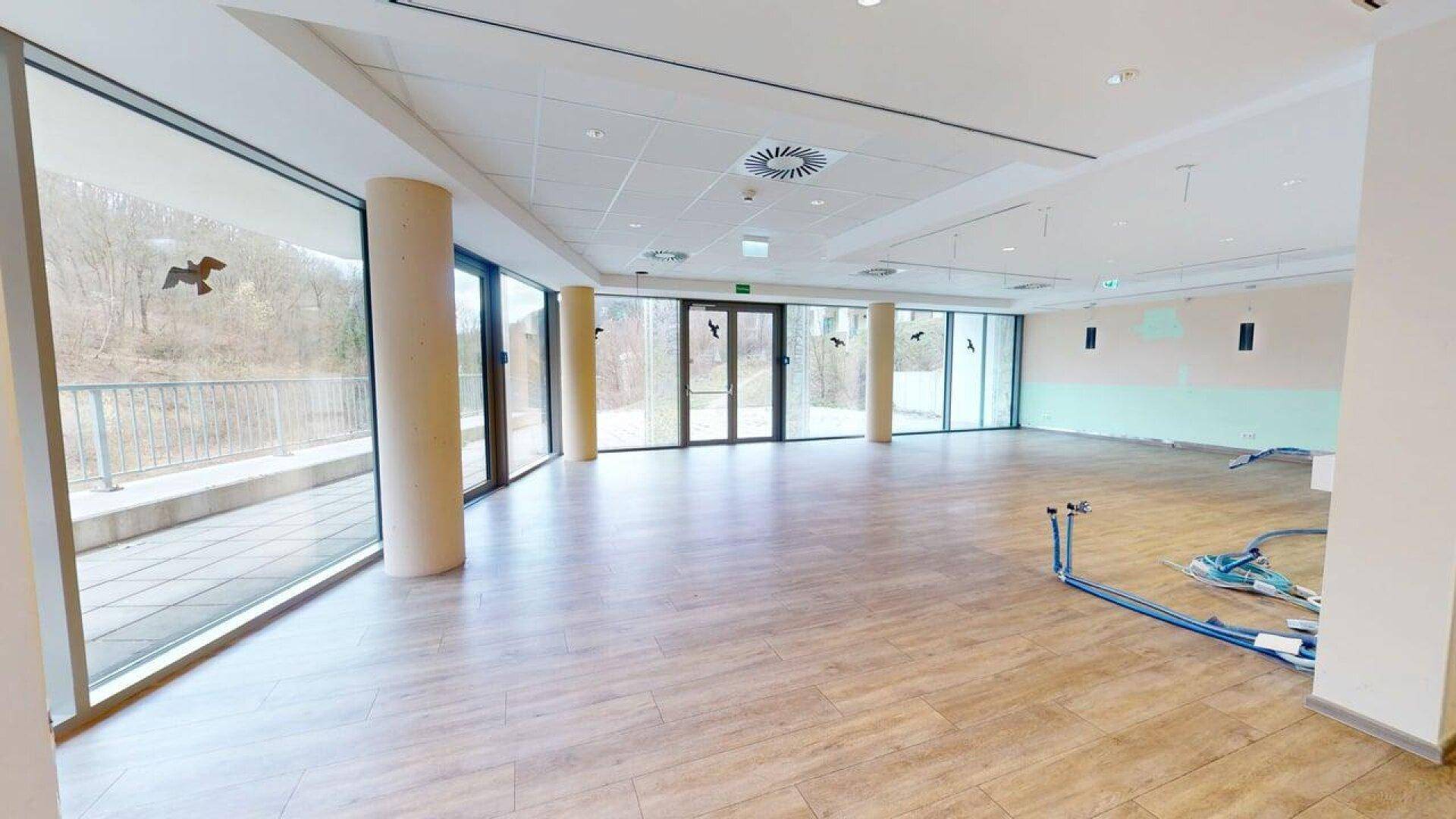 Großer, heller Gewerberaum mit Laminatboden und bodentiefen Fenstern, die auf eine Außenterrasse blicken.